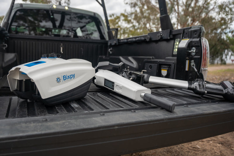 Bixpy electric outboard motor kit components, including the white battery pack and motor powerhead, resting in a pickup truck bed.