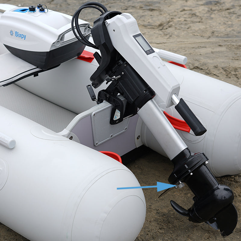 White Bixpy electric outboard motor and battery mounted on an inflatable boat on a sandy beach, with an arrow pointing to the anode.