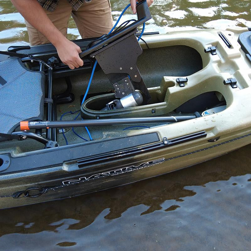 Person's hands installing a Bixpy Jet electric motor with a black adapter into the pedal well of a Native Watercraft kayak, in murky water.