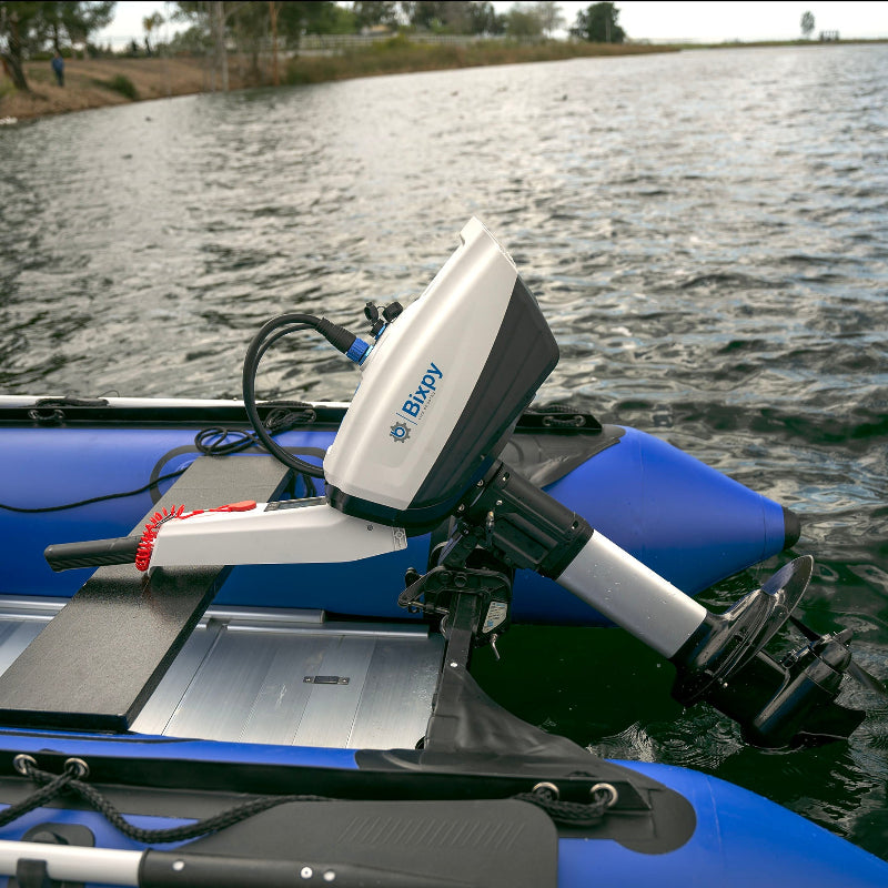 White Bixpy electric outboard motor with tiller handle mounted on a blue inflatable boat, propelling through rippled water.