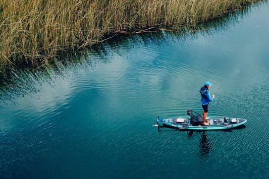 Man standing on personal watercraft powered by Bixpy K-1 in clear water as he fishes