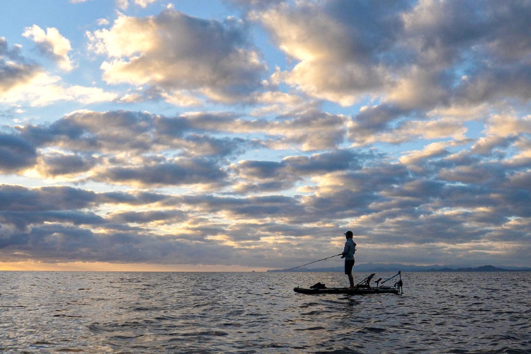 Man stands on personal watercraft at sunset, fishing with Bixpy Canada K-1 motor