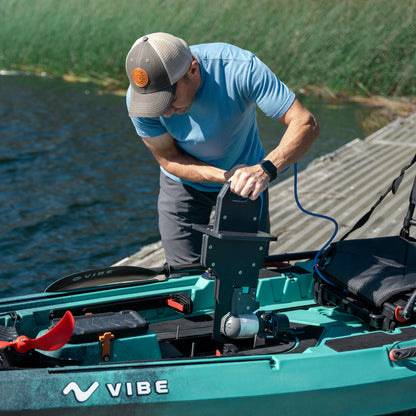 Man installing a Bixpy Jet electric motor with its black adapter into a teal Vibe kayak on a dock on the water.
