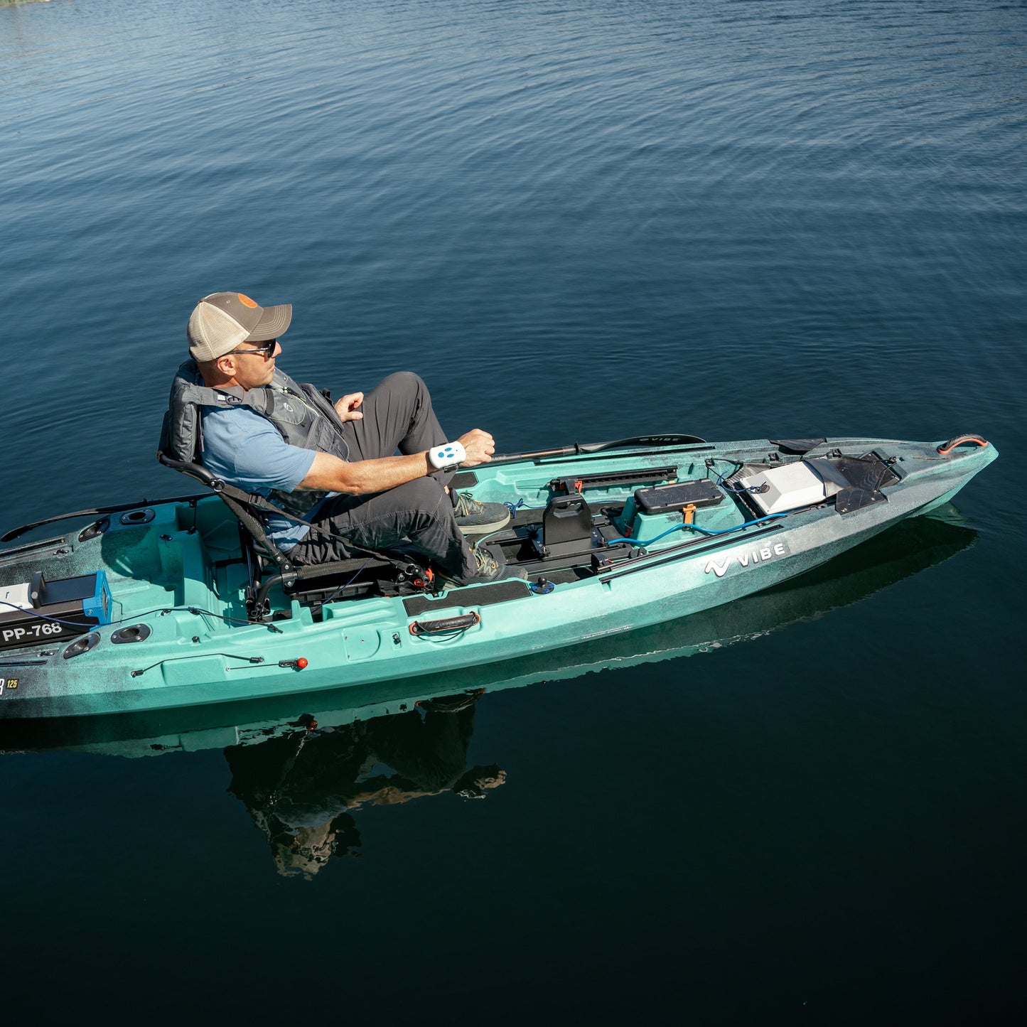 Man in a teal Vibe kayak, propelled by a Bixpy motor, moving across calm water, with a remote control visible on his wrist.