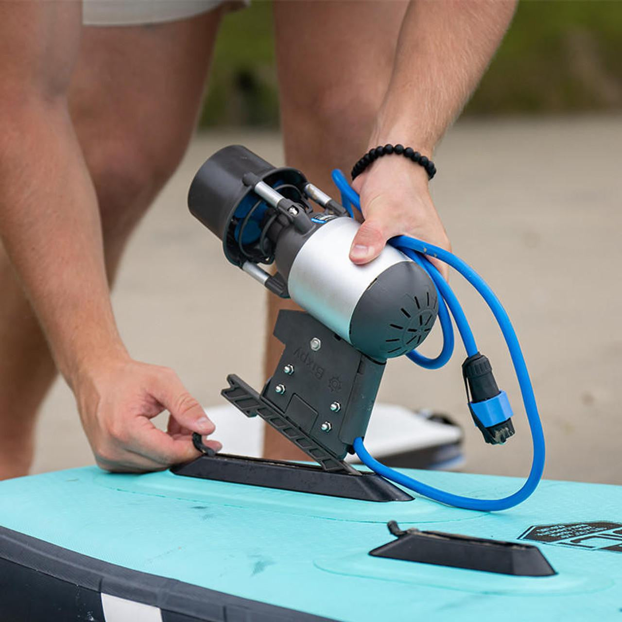 Person's hands inserting a Bixpy Jet electric motor and adapter into a light blue inflatable paddleboard.