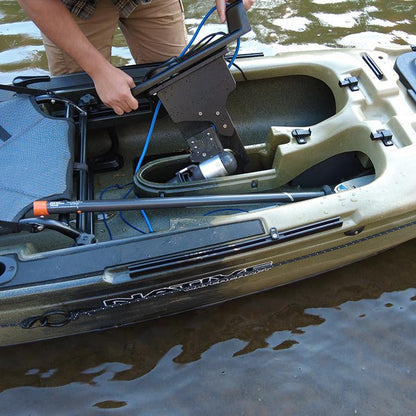 Person's hands installing a Bixpy Jet electric motor with a black adapter into the pedal well of a Native Watercraft kayak, in murky water.