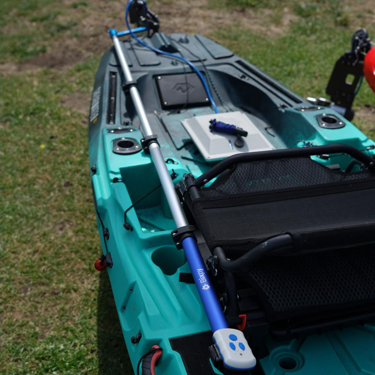 Bixpy Pole Steering™ system installed on a teal fishing kayak, featuring a long aluminum steering pole with a blue Bixpy handle mounted beside the seat, connected to the motor at the stern.