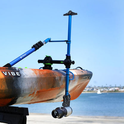 Orange and blue Vibe kayak with a Bixpy Jet electric motor mounted via a blue pole mount adapter, positioned above calm water with distant land and a sailboat.