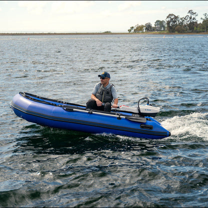 Man in a blue inflatable dinghy propelled by a white Bixpy electric outboard motor creating a large wake on rippled water.