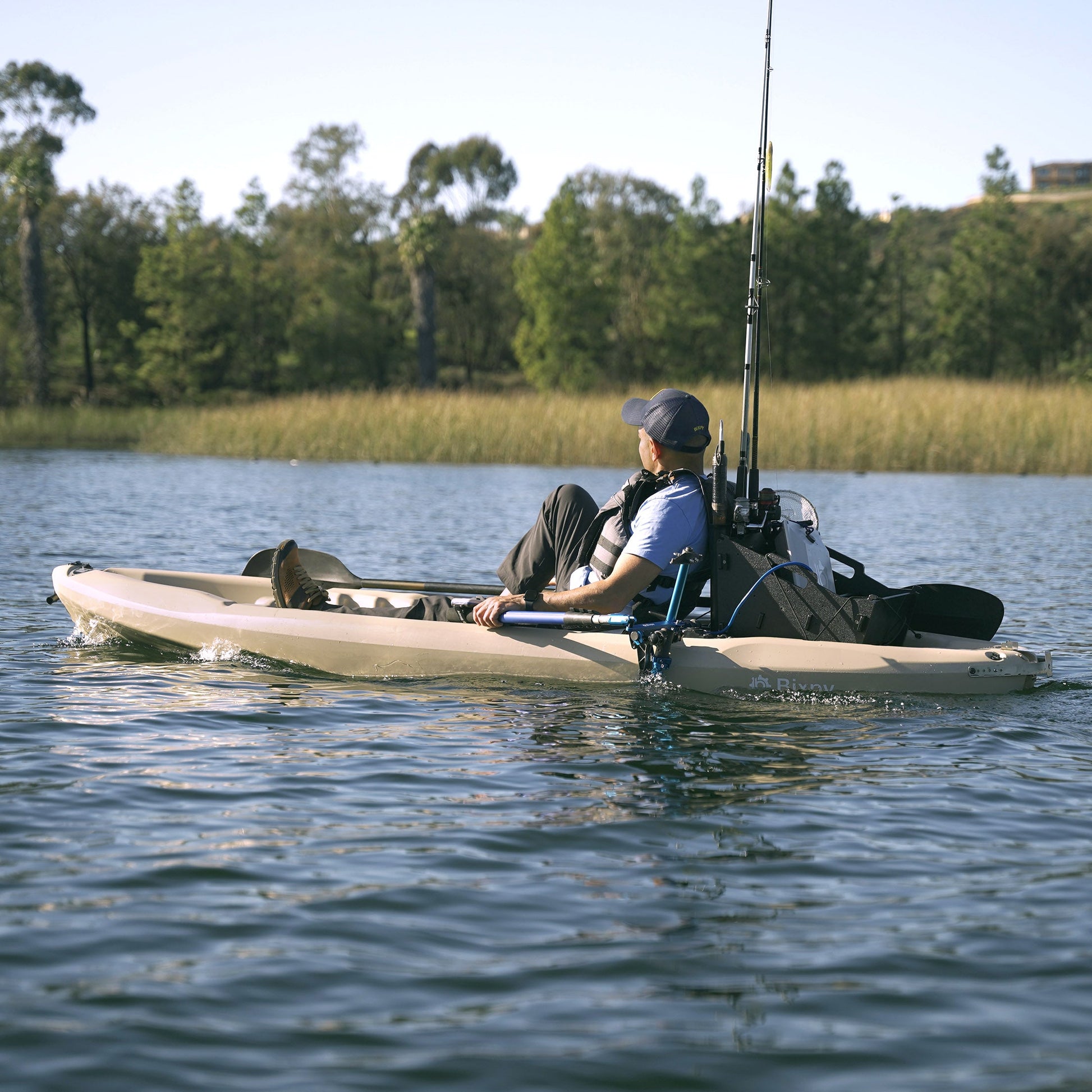 Person fishing from a kayak on a calm lake with trees in the background