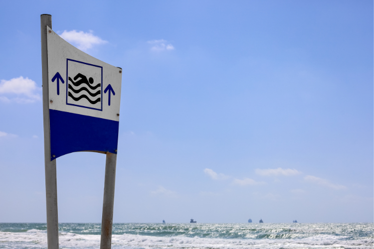 White and blue sign with a stick figure swimming in water and arrows pointing towards a swim zone